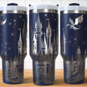 Puede incluir: Tazas de viaje azul marino con un dise&ntilde;o de castillo plateado, estrellas y un drag&oacute;n. Cada taza tiene una tapa blanca, un asa azul oscuro y un borde plateado. Las tazas miden aproximadamente 23 cm de alto.