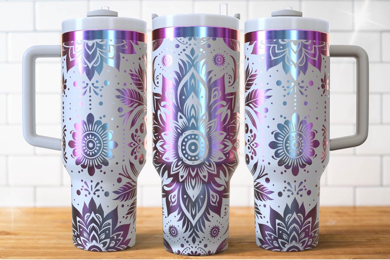 May include: Three white insulated tumblers with a floral mandala design in iridescent purple, blue, and pink. Each tumbler has a white handle and lid. The design features detailed flower and leaf patterns.