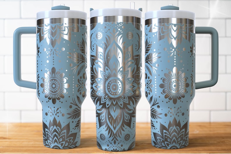 May include: Three stainless steel travel mugs with a light blue floral design. Each mug has a white lid, a light blue handle, and a silver floral pattern. The mugs are designed to keep beverages hot or cold.