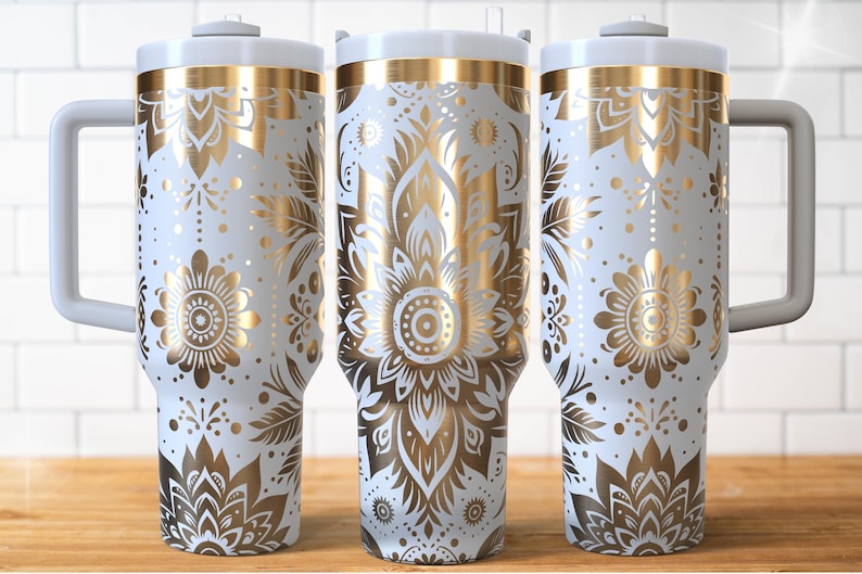 May include: Three white insulated tumblers with gold floral patterns and grey handles. The design features detailed gold flowers, leaves, and geometric shapes. Each tumbler has a white lid and a straw.