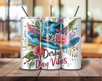 Puede incluir: Un vaso blanco con un diseño floral azul y rosa y un sombrero de vaquero azul. El texto "Derby Day Vibes" está impreso en el vaso.