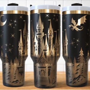 Puede incluir: Vaso de viaje negro con un dise&ntilde;o dorado de castillo, drag&oacute;n y bosque. El vaso tiene un asa negra, una tapa blanca y un borde dorado. El dise&ntilde;o incluye una luna y estrellas.