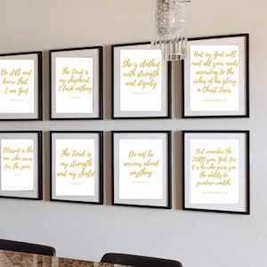 May include: A collection of eight framed art prints with gold script on white backgrounds. The black frames are hung on a white wall. The prints feature inspirational quotes from the Bible. The prints are arranged in two rows of four.