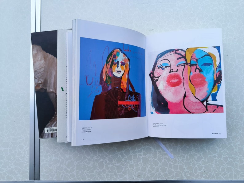 May include: Two pages from an art book featuring colourful abstract paintings of faces. The first page shows a woman with a red and black outfit against a blue background. The second page shows two faces with pink, blue and yellow paint.