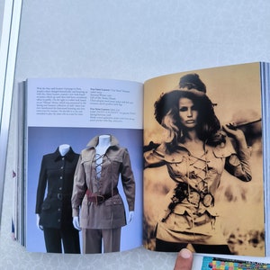 May include: Two models wearing safari-style jackets. The jacket on the left is black and has a button closure. The jacket on the right is brown with a lace-up front and a brown belt. The text "Yves Saint Laurent "City Farm"  Parfum" is visible in the image.