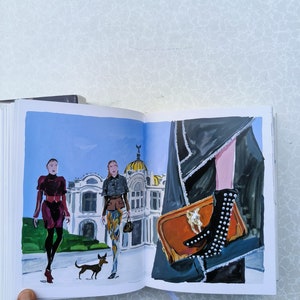 May include: An open book featuring an illustration of three people walking in front of a building. The people are wearing stylish clothing and one is holding a small dog. The other page shows a close-up of a brown leather handbag with a gold buckle and a black studded boot.