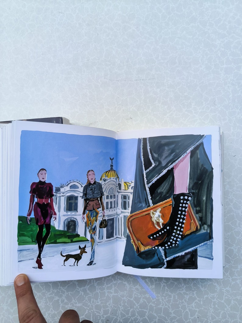May include: An open book featuring an illustration of three people walking in front of a building. The people are wearing stylish clothing and one is holding a small dog. The other page shows a close-up of a brown leather handbag with a gold buckle and a black studded boot.