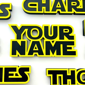 May include: Custom name signs in black and yellow with a Star Wars inspired font. The names include Chris, Charlie, Your Name, Thomas, James, and Mike.