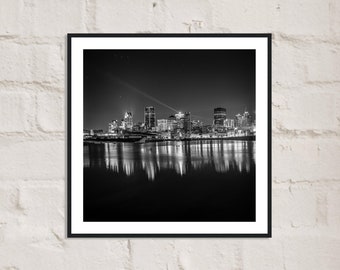 Puede incluir: Una fotografía en blanco y negro de un horizonte urbano de noche. La ciudad se refleja en el agua de abajo. Los edificios están iluminados, creando un hermoso contraste con el cielo oscuro.
