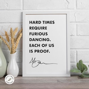 May include: Black and white typography print with the quote "Hard times require furious dancing. Each of us is proof." with a handwritten signature.