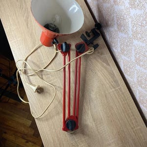 以下が含まれることがあります： クランプ付きの赤と白のデスクランプ。 ランプは円錐形のシェードとフレキシブルアームを備えています。 ランプは木製の表面にあります。