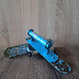 May include: Two vintage metal door handles featuring a distressed bright blue painted finish with visible wear and chipped paint revealing the dark metal underneath. Each handle has a cylindrical grip and a flat mounting plate with screw holes.