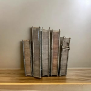 Könnte beinhalten: Eine Sammlung von sechs dekorativen, verwitterten Holzobjekten in Buchform. Die Objekte sind in einer Reihe angeordnet, mit verschiedenen Braun- und Grautönen. Ein Objekt hat einen kleinen Stuhl daran befestigt. Die Objekte stehen auf einem Holzregal.