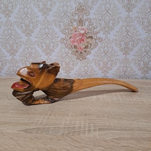 May include: A wooden lizard-shaped nutcracker with an open mouth and a red tongue. The lizard is carved from wood and has a long, curved handle. The nutcracker is brown and has a detailed design.