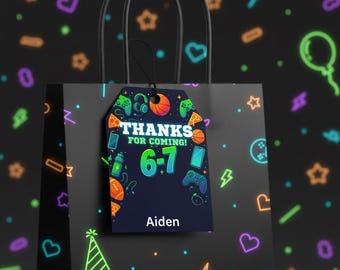 Può includere: Una borsa regalo nera con un'etichetta che dice "THANKS FOR COMING!" e "6-7" con il nome "Aiden". L'etichetta presenta grafiche a tema gaming come un controller, cuffie e pizza. Lo sfondo è nero con forme al neon.