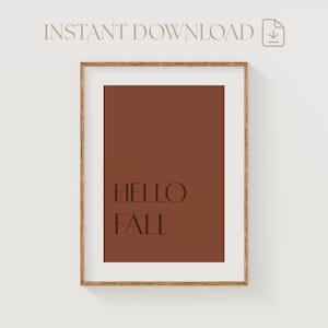 May include: A framed print featuring a deep brown background with the words "HELLO FALL" in a serif font. The frame is a light brown colour. The words "INSTANT DOWNLOAD" are at the top.