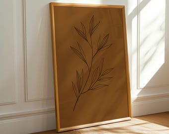 May include: A framed botanical art print featuring a minimalist line drawing of a plant stem with leaves. The artwork is set against a warm brown background and framed in a light wood frame. The print leans against a white wall and wooden floor.