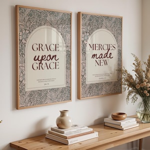 Könnte beinhalten: Zwei gerahmte Kunstdrucke mit Holzrahmen. Die Drucke zeigen florale Muster und die Sätze "GRACE upon GRACE" und "MERCIES made NEW" in burgunderrotem Text. Die Drucke werden über einem Holzkonsolentisch angezeigt.