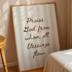 May include: A framed print with the words "Praise God from whom all blessings flow" in a brown script font. The background has vertical stripes in shades of white and beige. The frame is made of light-colored wood.