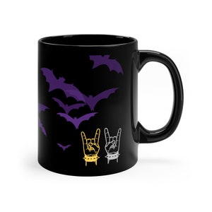 May include: Black ceramic coffee mug with a design of purple bats flying in a dark sky and two gold and silver rock and roll hand gestures.
