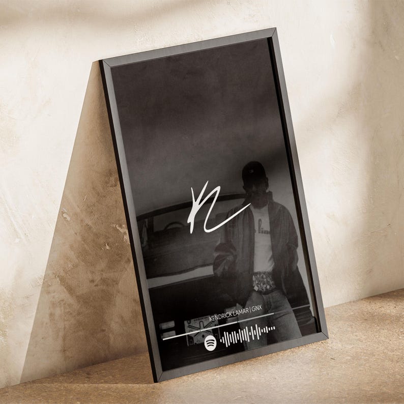 Puede incluir: P&oacute;ster enmarcado en blanco y negro con una persona con gorra de b&eacute;isbol. El p&oacute;ster incluye una firma blanca y el texto "KENDRICK LAMAR | GNX" con una forma de onda de audio de Spotify. El marco es negro.