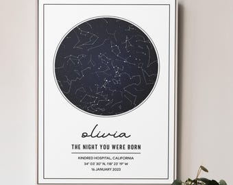 Puede incluir: Impresión enmarcada con un mapa estelar circular azul oscuro. La impresión incluye el nombre "olivia" en cursiva, el texto "THE NIGHT YOU WERE BORN" y detalles de ubicación y fecha. El marco es blanco.