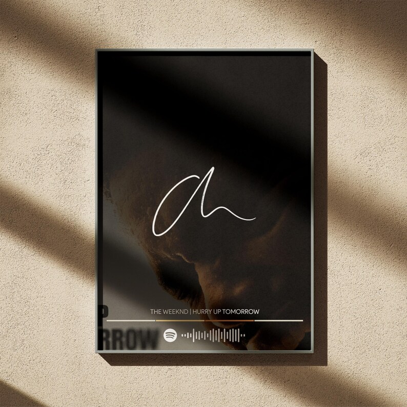 Puede incluir: Impresi&oacute;n art&iacute;stica enmarcada con fondo negro, una "a" blanca en cursiva y una imagen borrosa. El texto "THE WEEKND | HURRY UP TOMORROW" se muestra debajo, junto con un c&oacute;digo de Spotify. Marco oscuro.