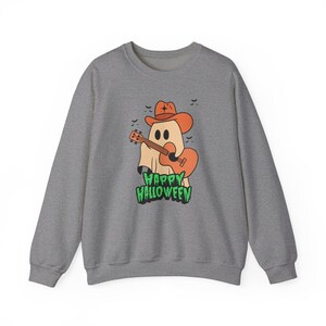 Peut inclure: Un sweat-shirt gris chiné à col rond orné d'un motif représentant un fantôme portant un chapeau de cowboy orange et jouant d'une guitare acoustique orange. De petites chauves-souris noires entourent le fantôme et le texte HAPPY HALLOWEEN est en vert.
