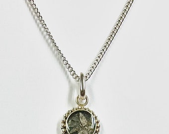 May include: A silver necklace with a round pendant. The pendant has a textured, gray and green stone set within a beaded silver frame. The chain is a curb style, and the necklace is displayed against a white background.