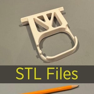 Könnte beinhalten: Zwei 3D-gedruckte weiße Kunststoffhalter für eine Toilettenpapierrolle. Der obere Halter ist von der Wand abgezogen, während der untere Halter bündig mit der Wand ist. Ein Bleistift liegt neben dem unteren Halter zur Skalierung.