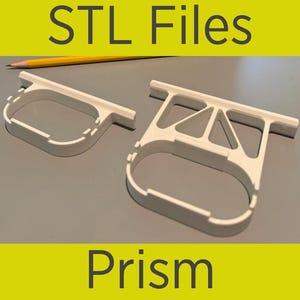 Puede incluir: Dos modelos de prisma blancos impresos en 3D con un lápiz en el fondo. Los modelos tienen forma de rectángulo curvo con la parte superior plana. El texto "STL Files" está en la parte superior y "Prism" en la inferior.