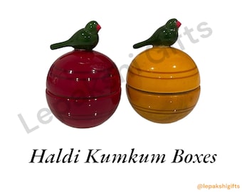 May include: Two wooden boxes with bird lids. The boxes are round and have a red and yellow finish. The lids are shaped like birds with green bodies and red beaks. The boxes are labeled "Haldi Kumkum Boxes".