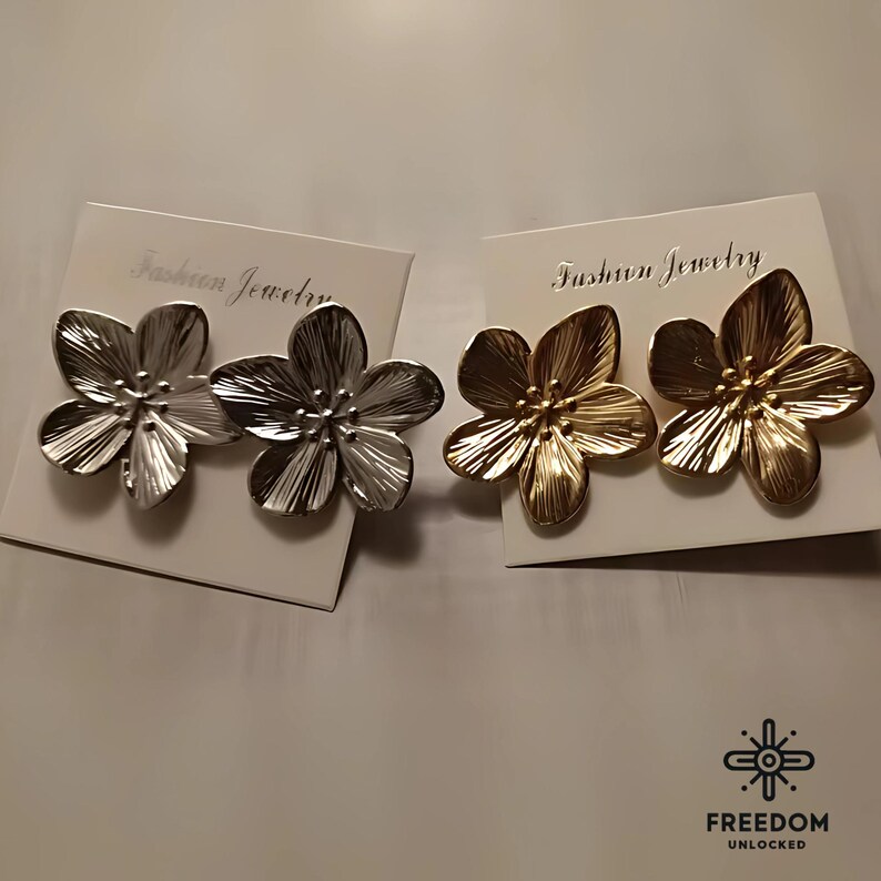 Op de afbeelding: Twee paar bloemvormige oorbellen, &eacute;&eacute;n paar is goud en het andere is zilver. De oorbellen liggen op een witte kaart met de tekst "Fashion Jewelry" erop gedrukt.