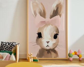 May include: A framed art print featuring a bunny with a pink bow. The bunny has brown and white fur, large black eyes, and a pink background. The frame is a light wood color. The artwork is displayed in a child's room.