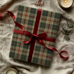 May include: A wrapped gift with a green plaid pattern, accented with red and beige lines. A deep red satin ribbon is tied in a bow around the gift. The gift is on a neutral-colored fabric background.