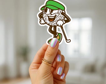 May include: A cartoon golf ball character sticker with a green cap, shoes, and golf club. The golf ball has a smiling face and is walking. The sticker is held by a hand with gold rings and iridescent nail polish.