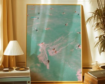 May include: A framed art print featuring an aerial view of surfers in the ocean. The water is a vibrant turquoise color, with white waves and numerous surfers riding the waves. The print is in a gold frame.