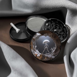 May include: A black metal herb grinder consisting of four circular components, including a lid featuring a circular graphic of a white mushroom-like figure in a cave, a mesh screen, a grinding chamber with teeth, and a small white plastic scraper.