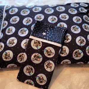 May include: Two pillowcases, one rectangular and one folded, featuring a dark blue background with a repeating pattern of a space ranger character in a circular design. The folded pillowcase has a blue star pattern.