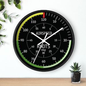 May include: Black and green clock with white hands and a black bezel. The clock face has a white background with black markings and the text "AIRSPEED" and "KNOTS Clockz".