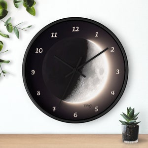 May include: A black wall clock with a crescent moon design. The clock face has white numbers and a black background. The moon is illuminated with a white glow.