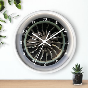 May include: White round wall clock with a jet engine design. The clock face has black numbers and white hands.