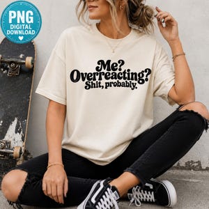 May include: A cream-colored short-sleeve t-shirt featuring black text printed on the front that reads, "Me? Overreacting? Shit, probably." The shirt has a crew neckline and a relaxed fit, paired with black distressed jeans and black sneakers.