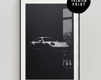 May include: A black and white photograph of a silver sports car parked in a garage. The car is partially obscured by a window and some foliage.