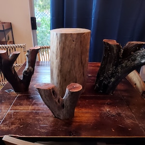 Puede incluir: Cuatro piezas de madera natural, incluyendo un cilindro grande y tres piezas más pequeñas en forma de V, están dispuestas sobre una mesa de madera marrón oscuro.