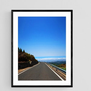 Könnte beinhalten: Eine kurvenreiche asphaltierte Straße führt bergauf mit blauem Himmel und weißen Wolken in der Ferne.
