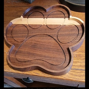 May include: A wooden paw print tray with five circular indentations. The tray is made of dark brown wood with a lighter brown wood inlay.