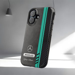 Op de afbeelding: Zwarte telefoonhoes met een koolstofvezeltextuur en turquoise strepen. De hoes heeft het Mercedes-Benz-logo, AMG-branding en de tekst "Your Name". De hoes is ontworpen om de telefoon te beschermen.