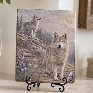 May include: A rectangular decorative tile featuring a detailed illustration of two grey wolves in a mountainous landscape. One wolf stands on a rocky ledge while the other stands in the foreground. A full moon shines in the sky above pine trees.