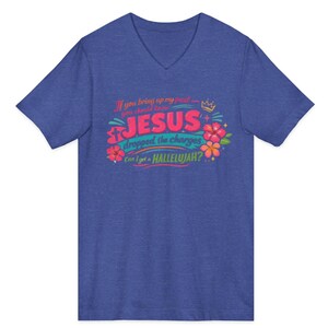 Puede incluir: Una camiseta azul con cuello en V que presenta un estampado gr&aacute;fico con el texto: If you bring up my past you should know JESUS dropped the charges Can I get a HALLELUJAH? El dise&ntilde;o incluye una peque&ntilde;a corona, una cruz y flores de hibisco.